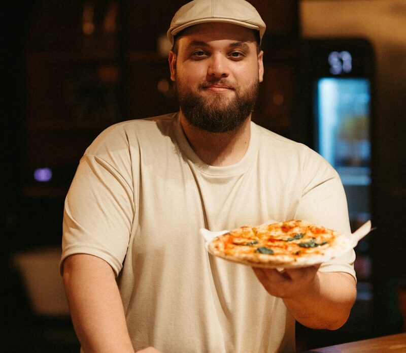 a man holding a pizza on top of a wooden counter
